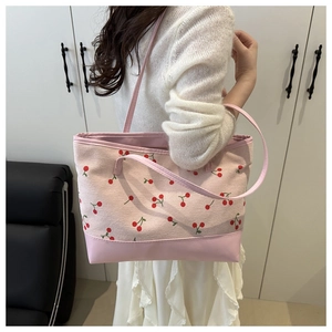 Detail view of pink tote bag with red cherry print and reinforced leather bottom on model