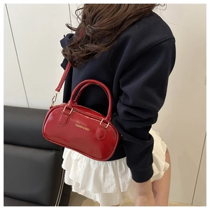 Detailed view of a shiny red patent leather crossbody bag with top handles on a model