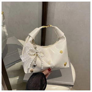 Détail du sac à main en cuir verni blanc avec rivets dorés et breloque en dentelle