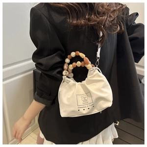 Detail of cream bucket bag featuring colorful beaded handle and bear logo label