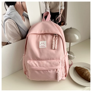 Detailed view of pink backpack with smiley patch and woven zipper pull on a desk