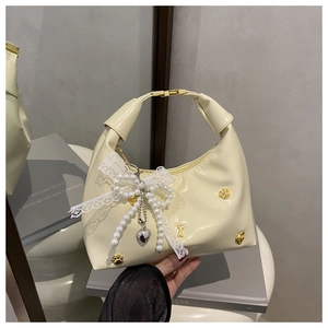 Détail du sac demi-lune blanc cassé avec nœud en dentelle et pendentifs cœur