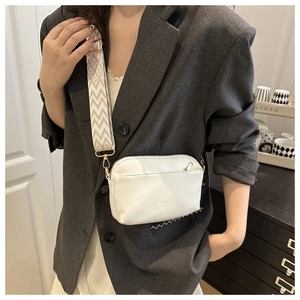 Detail of white crossbody bag featuring a wide woven jacquard strap and gold hardware