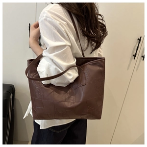 Detail of dark brown tote bag with crocodile texture worn over shoulder by model
