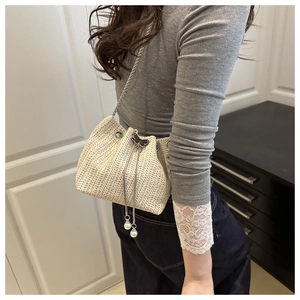 Detail of woven straw bucket bag with metal chain, black bow, and pearl tassels