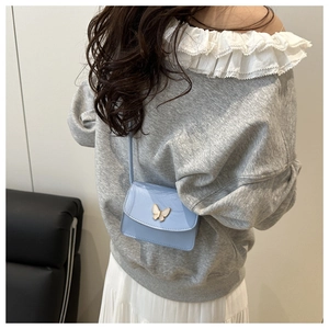 Detail of light blue crossbody bag featuring a golden butterfly buckle and glossy leather