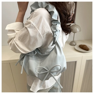 Close-up of light blue shoulder bag with bow detail and pleated handle texture