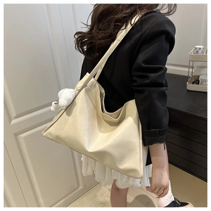 Detail of a large off-white tote bag in glossy leather worn by a model with plush charm