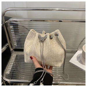 Detailed shot of beige straw bucket bag featuring a butterfly buckle and pearl drawstring