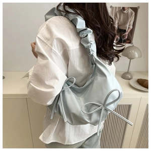 Detail of light blue pleated shoulder bag featuring a large bow and ruched strap design