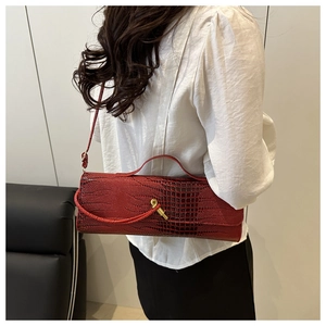 Détail d'un sac baguette rouge foncé avec texture crocodile et fermoir rotatif en métal doré