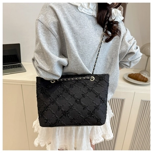 Detail of black quilted tote bag with metallic chain strap in a casual lifestyle setting