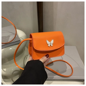 Detail of a vibrant orange square crossbody bag featuring a cream butterfly ornament