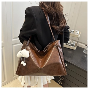 Detail of a large dark brown faux leather tote bag with a plush cloud charm on model