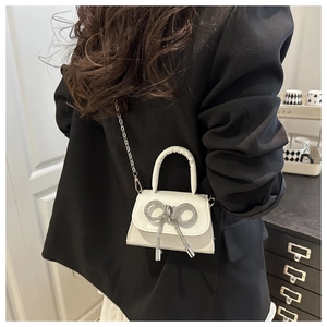 Détail d'un mini sac à main blanc avec nœud en cristaux et bandoulière en chaîne
