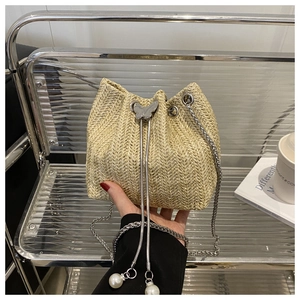 Detail of straw bucket bag featuring silver butterfly ornament and pearl drawstring