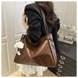 Detail of dark brown glossy oil-wax leather tote bag with white cloud plush pendant