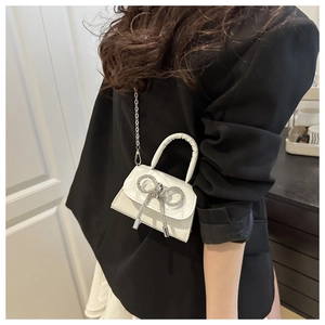 Détail d'un mini sac en cuir blanc avec nœud en strass et chaîne argentée
