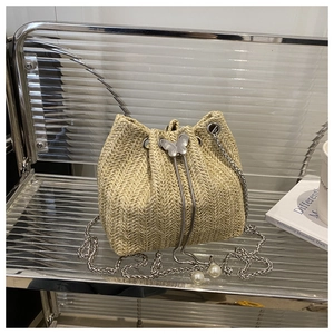 Macro detail of beige woven straw bucket bag with drawstring and pearl metal chain