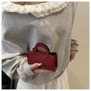 Close-up of red crocodile pattern mini handbag with round handle held by a model