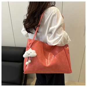Detail of coral orange leather tote bag with cloud charm on modern sofa background