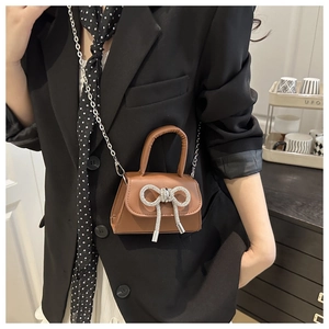 Détail d'un mini sac bandoulière en cuir marron avec nœud en strass argentés et chaîne