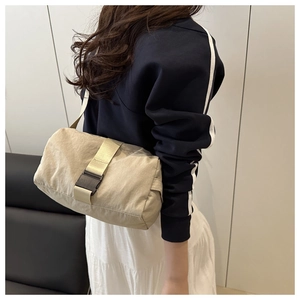 Model wearing a beige textured oxford fabric shoulder bag with a black buckle detail