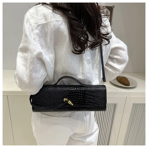 Détail du sac baguette cylindrique noir avec texture crocodile et boucle dorée chic