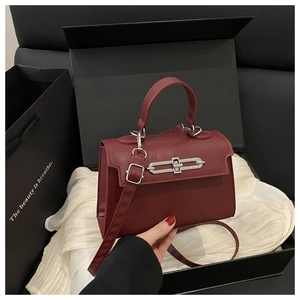 Détail d'un sac carré bordeaux avec fermoir argenté dans un coffret cadeau de luxe