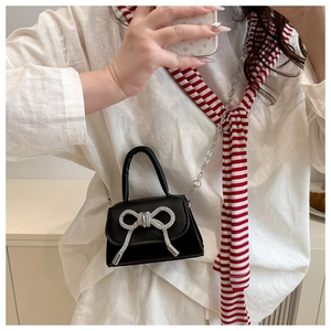 Détail d'un mini sac à main en cuir noir avec un grand nœud en strass argentés et une chaîne