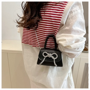 Détail d'un sac à main noir avec un nœud en strass argentés et une bandoulière chaîne