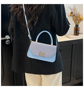 Detail of light blue woven leather handbag with gold metal logo worn with black blazer