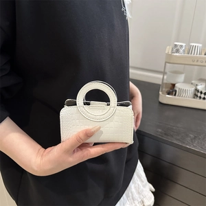 White faux crocodile pattern mini handbag with round handle held in hand for scale