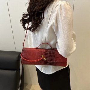Sac baguette rouge foncé avec relief crocodile et fermoir doré porté à l'épaule
