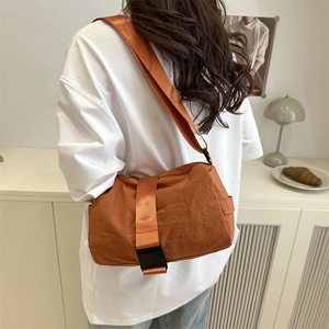 Modern orange nylon crossbody bag with buckle closure worn by a model in casual setting