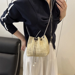 Straw woven bucket bag with chain strap and pearl drawstring detail on a model