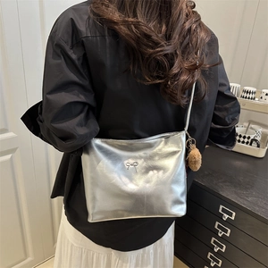 Silver metallic crossbody bag with bow detail and plush ball pendant worn by a model
