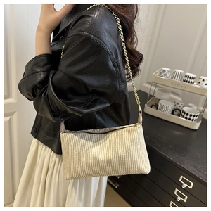 Detail of beige woven pillow bag with gold chain strap worn by a model in black leather jacket