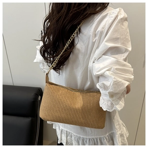 Detailed view of light brown woven pillow bag with a gold chain strap on a model