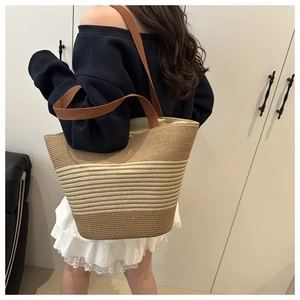 Detail view of woven straw bucket bag with brown and beige stripes and wide shoulder strap