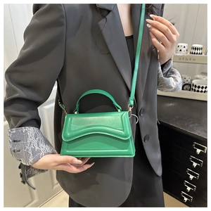 Detail of green leather handbag featuring wave pattern flap and elegant gold hardware