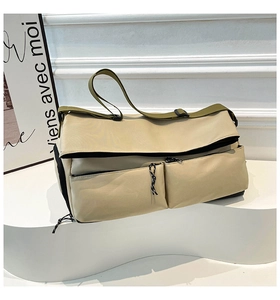 Close-up of a large beige crossbody bag with olive green straps and dual side pockets