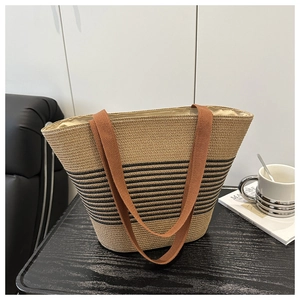 Dettaglio della borsa tote in paglia intrecciata a righe nere su un tavolo di legno