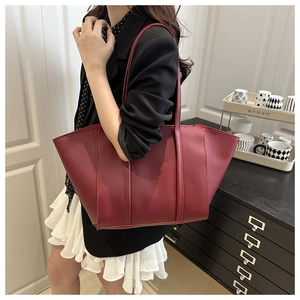 Model wearing large burgundy faux leather tote bag in a minimalist interior setting