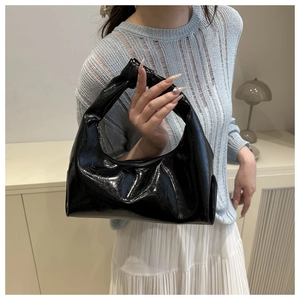 Dettaglio di una borsa hobo nera lucida con manico a nodo in un ambiente domestico