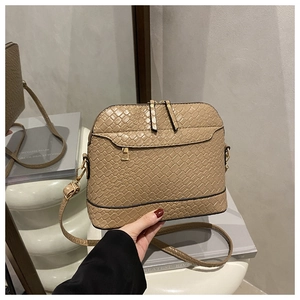 Close-up of khaki woven shell bag with gold double zippers on a modern pedestal