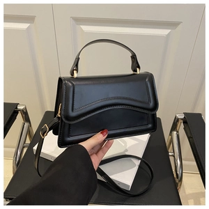 Detail of black glossy leather handbag with wave stitching and gold hardware accents