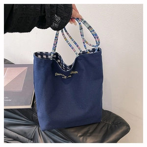 Close-up of navy canvas tote bag with striped woven handles and gold logo embroidery