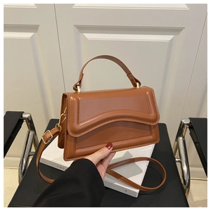Detail of caramel leather handbag with wavy textured flap and gold-tone metal hardware