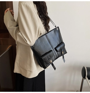 Close-up of black leather square tote bag featuring dual front pockets and metal buckles